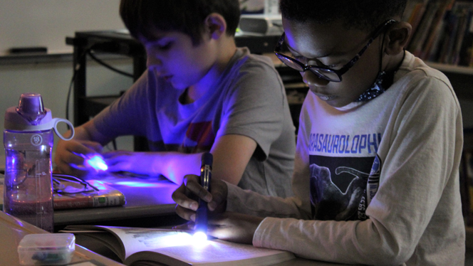 Students reading in the dark with flashlights.