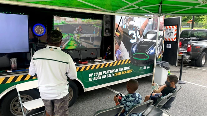 People playing Mario Kart at an outdoor gaming station. People playing Mario Kart at an outdoor gaming station.