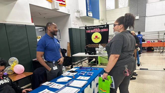 Staff at Brooklyn Scholars charter school fair booth talks with parent