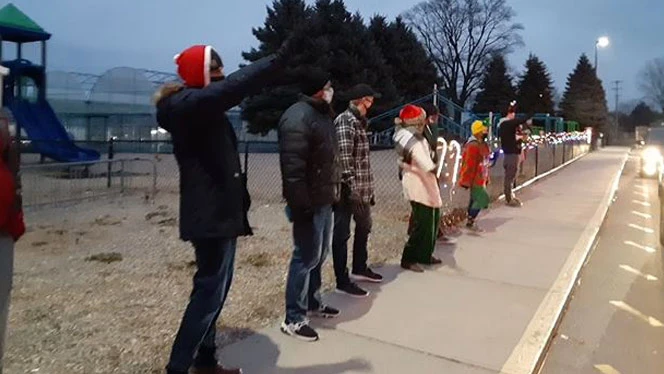 Adults bundled up and waving to vehicles. Adults bundled up and waving to vehicles.