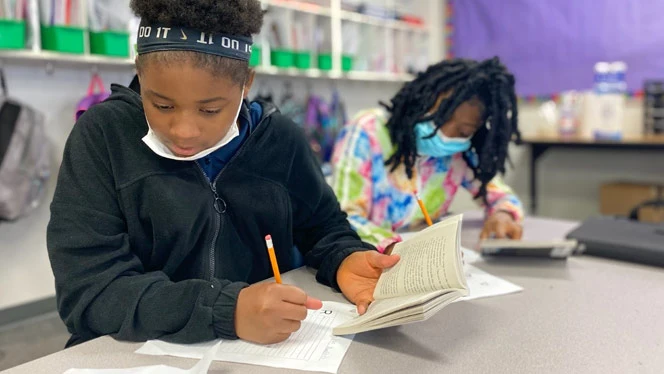 Students reading and writing at a table. Students reading and writing at a table.