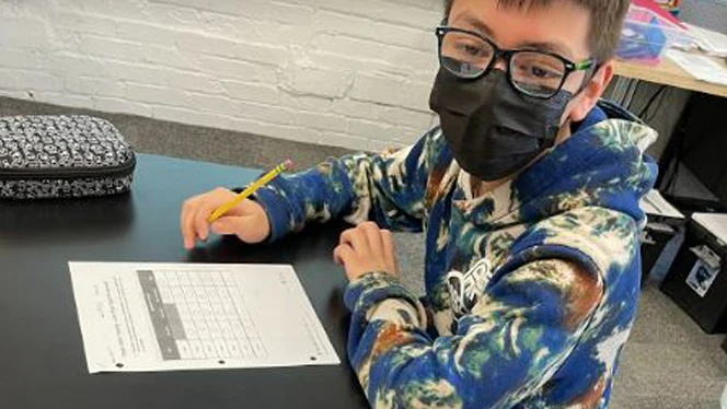 Student writing at a table. Student writing at a table.
