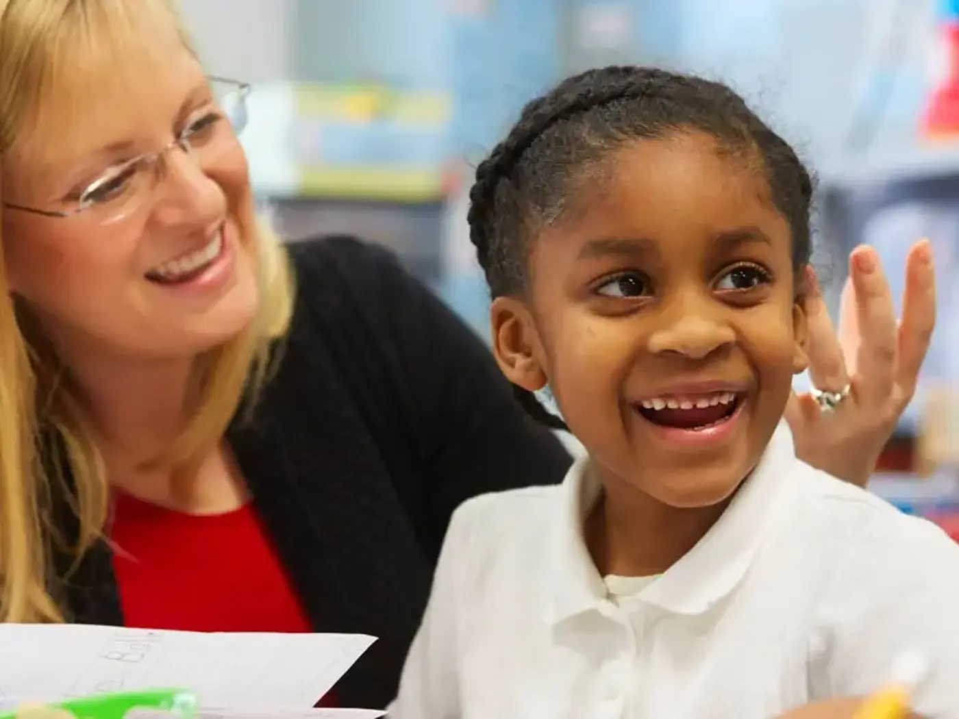 K-12 School in Center Line: Teacher and student smiling at desk.