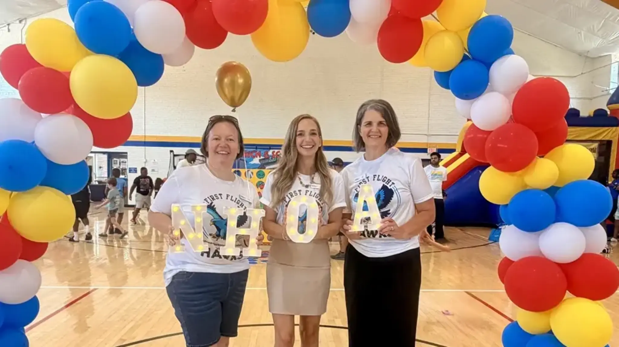 a group of women holding letters in front of a balloon arch