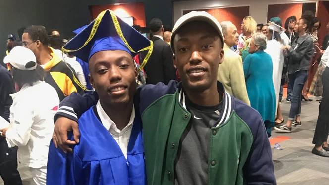 A man in a graduation cap smiling with another man. A man in a graduation cap smiling with another man.