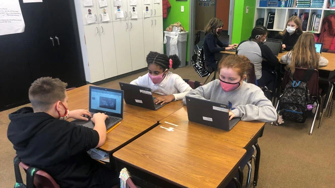 students at a table learning on their laptops students at a table learning on their laptops