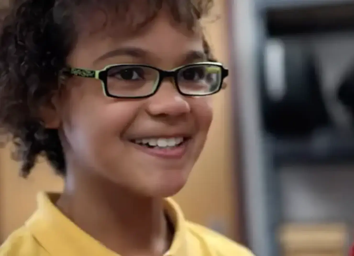Student with yellow shirt and glasses smiling.