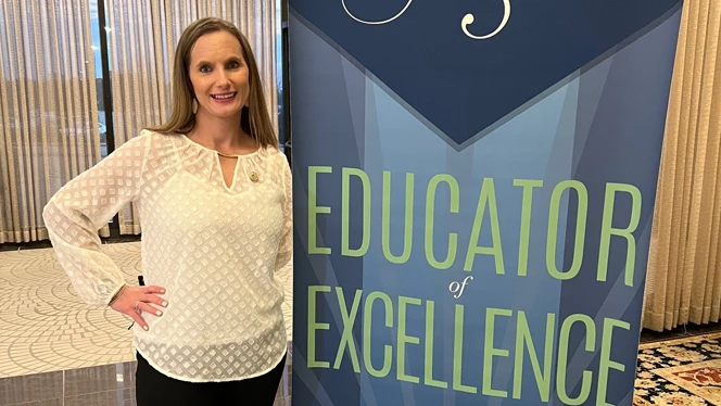 Woman standing next to sign that says Educator of Excellence. Woman standing next to sign that says Educator of Excellence.