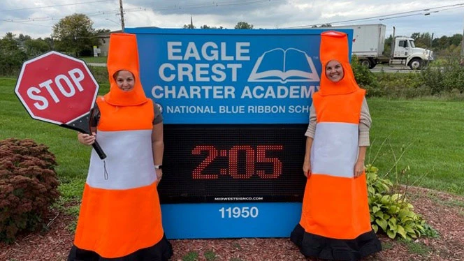 People dressed as traffic cones holding a stop sign. People dressed as traffic cones holding a stop sign.