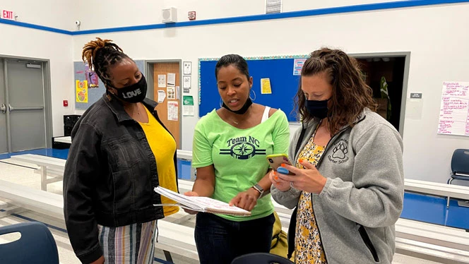 Three people reading from a notebook.
