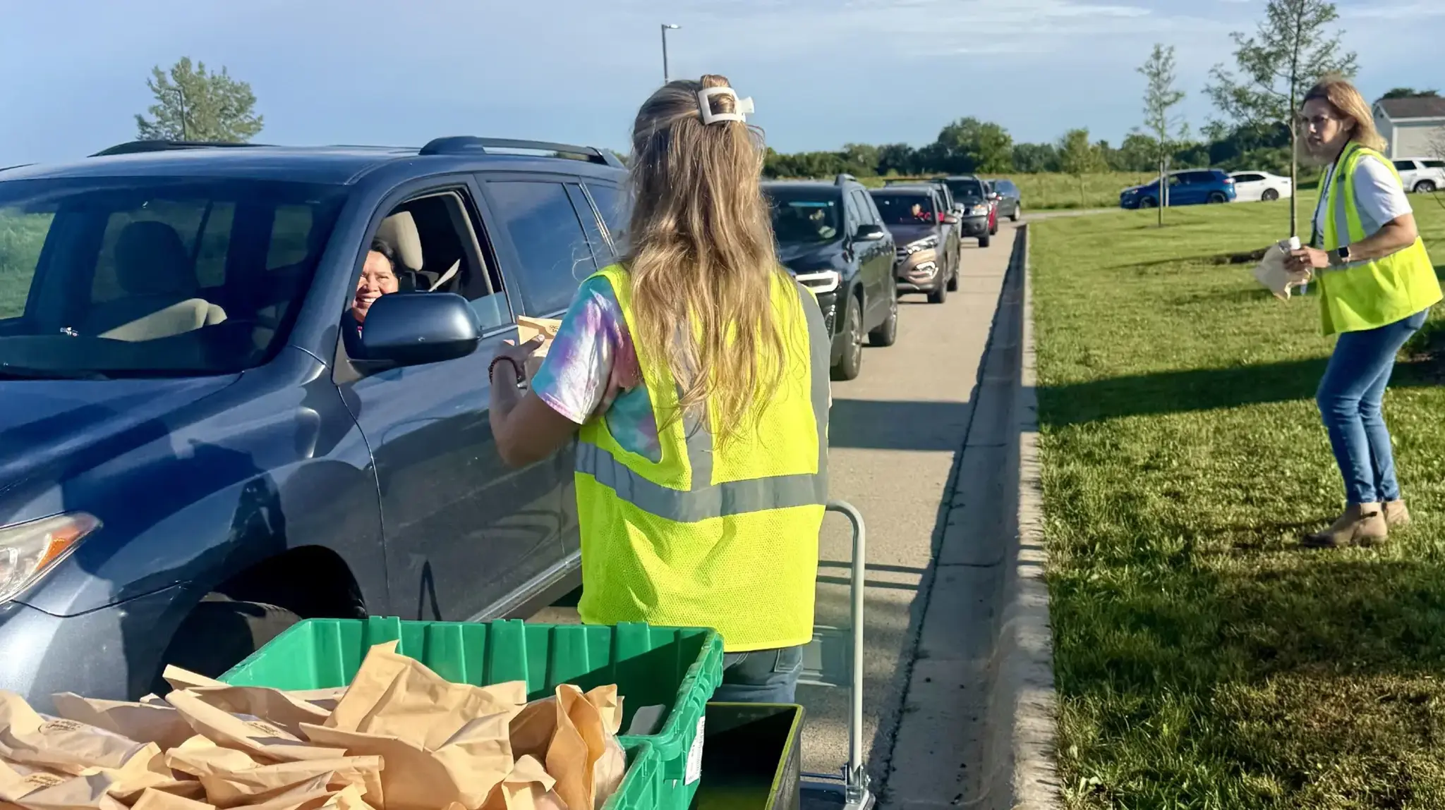 a woman in a yellow vest standing in a car with a cart and a green basket