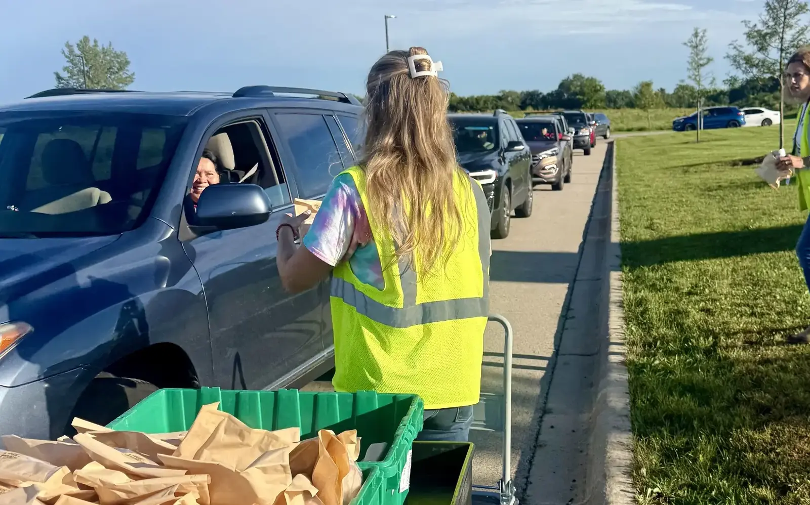 a woman in a yellow vest standing in a car with a cart and a green basket