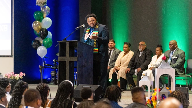Dr Hall speaking on a stage. Dr Hall speaking on a stage.