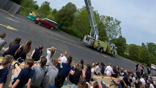 Students sitting on a curb watching a fire truck. Students sitting on a curb watching a fire truck.