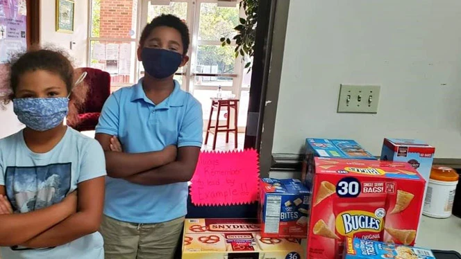 Children standing with arms folded next to boxes of food Children standing with arms folded next to boxes of food