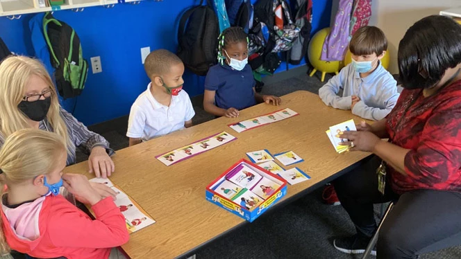 Students and teachers playing a game at a table. Students and teachers playing a game at a table.