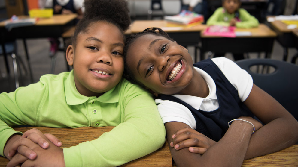 Two students smiling in front of their classroom lockers