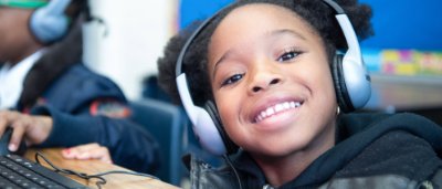 Brooklyn Excelsior Charter School, K-8 School in Brooklyn, NY: student wearing headphones, smiling.