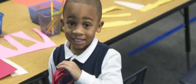 K-8 School in Canton: Student smiling at desk with paper craft.