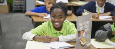 K-8 School in Detroit: Student smiling at desk, doing assignment.