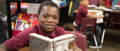 K-8 School in Gary: Student sitting at desk with book, smiling.