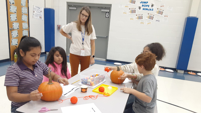 Students crafting with pumpkins at a table.