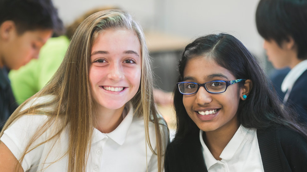 Two students smiling in front of their classroom lockers