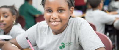 Brooklyn Scholars Charter School, K-8 School in Brooklyn, NY: girl in a grey t-shirt holding a pink pencil and smiling.