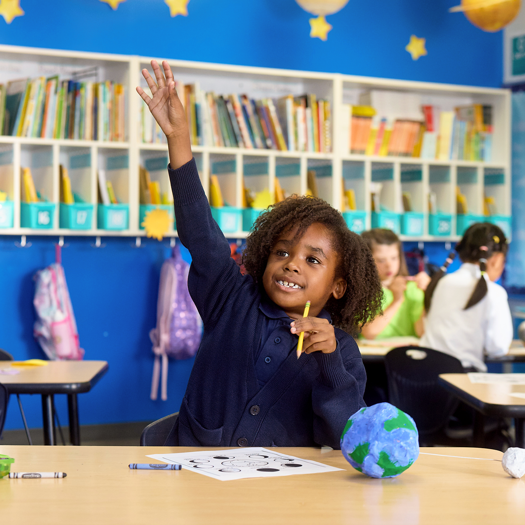 Elementary student in class with hand up.