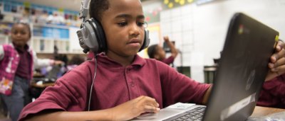 K-8 School in Gary: Student using headphones and working on laptop at desk.