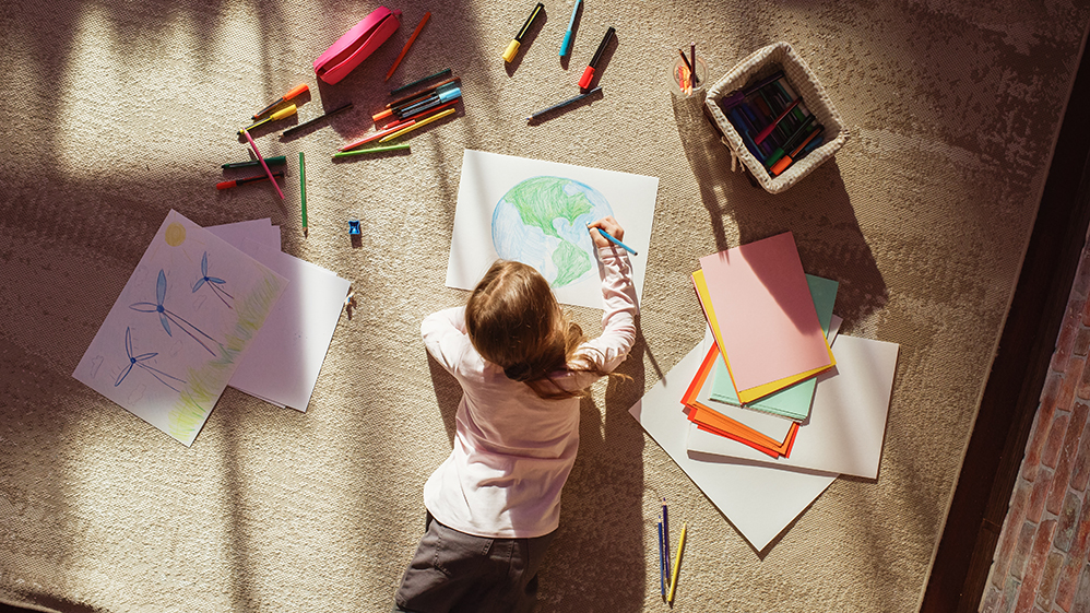 Child laying on the floor coloring with crayons.