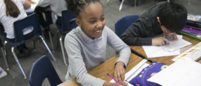 K-8 School in Canton: Student smiling at desk doing classwork.
