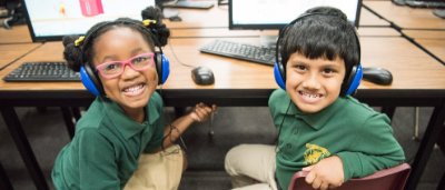 Brooklyn Scholars Charter School, K-8 School in Brooklyn, NY: two young students sitting at computers, turned around and smiling.