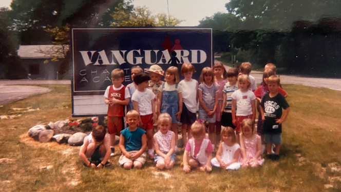 A faded photograph of students standing in front of Vanguard sign.