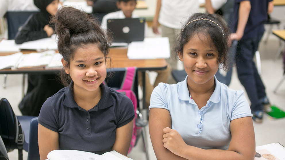 Two students smiling in front of their classroom lockers