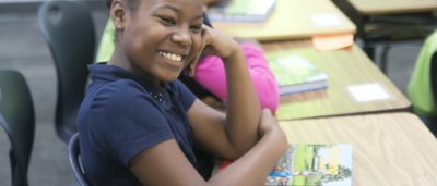 K-8 School in Detroit: Student smiling at desk with book.