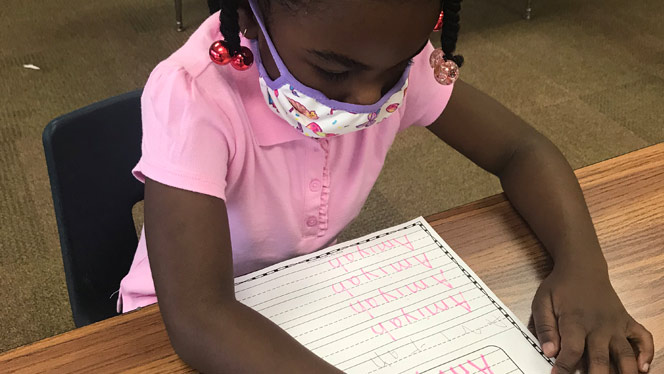 Student learning letters at a table.