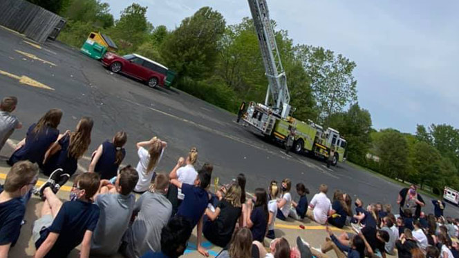 Students sitting on a curb watching a fire truck.