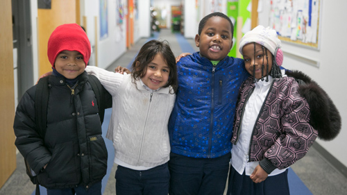 Group of multi-national students standing in a hallway with arms around each other.